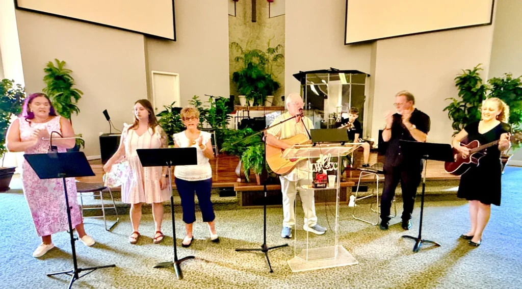 Worship team leading praise outdoors in 90 degree heat at Living Waters Christian Community, August 9, 2026