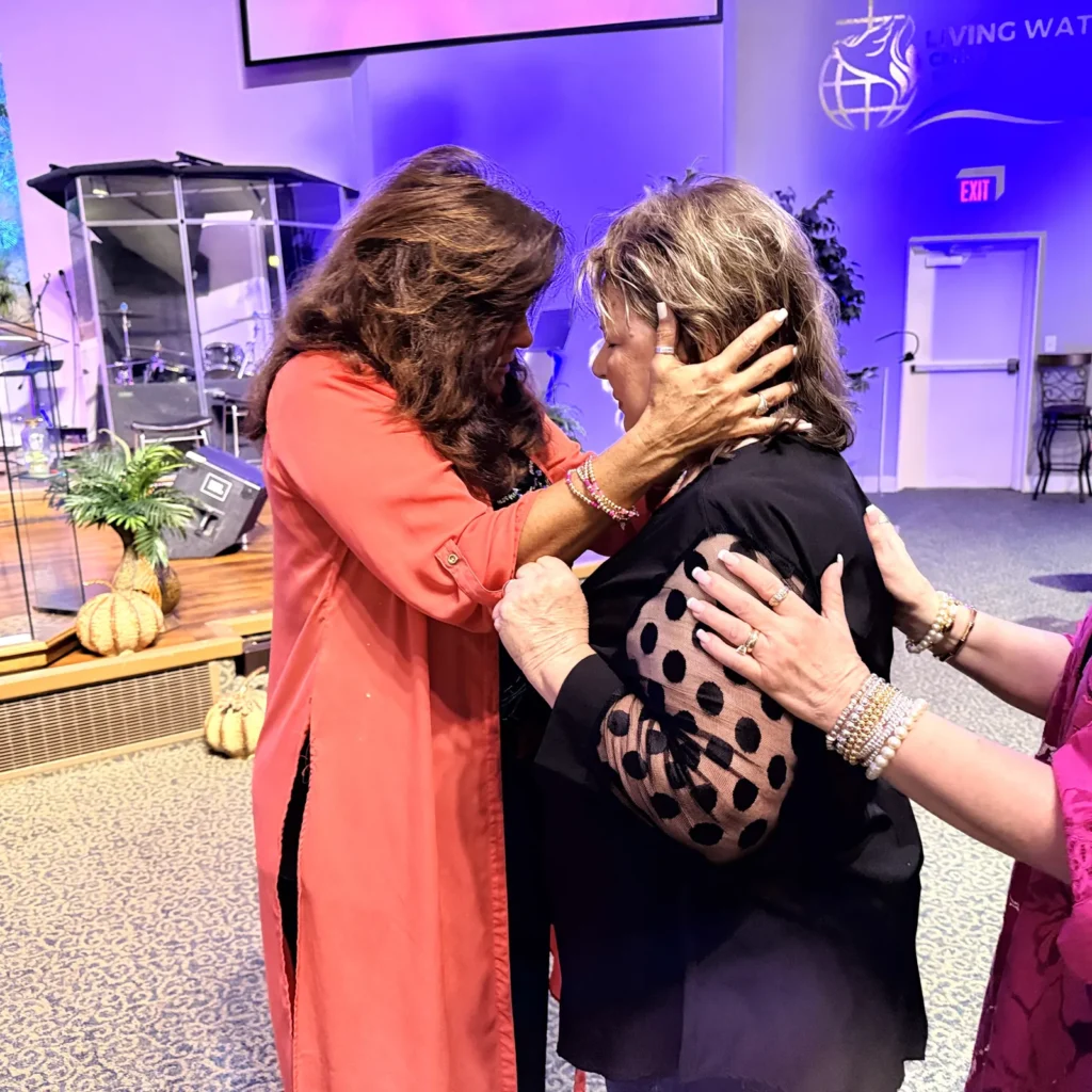 Women praying together and laying hands on one another at the front of the Living Waters sanctuary