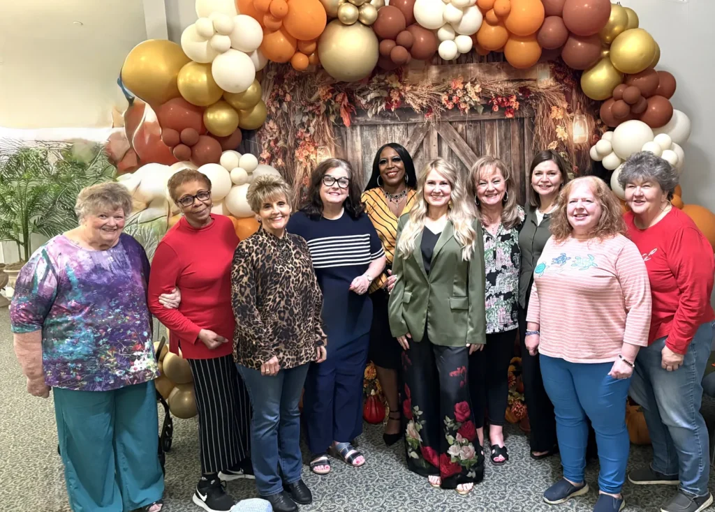 Daughters of Zion women gathered for a group photo in front of an autumn balloon arch and rustic barn door backdrop