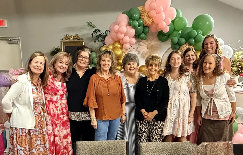 Daughters of Zion women smiling together in front of a pink, green and gold balloon arch